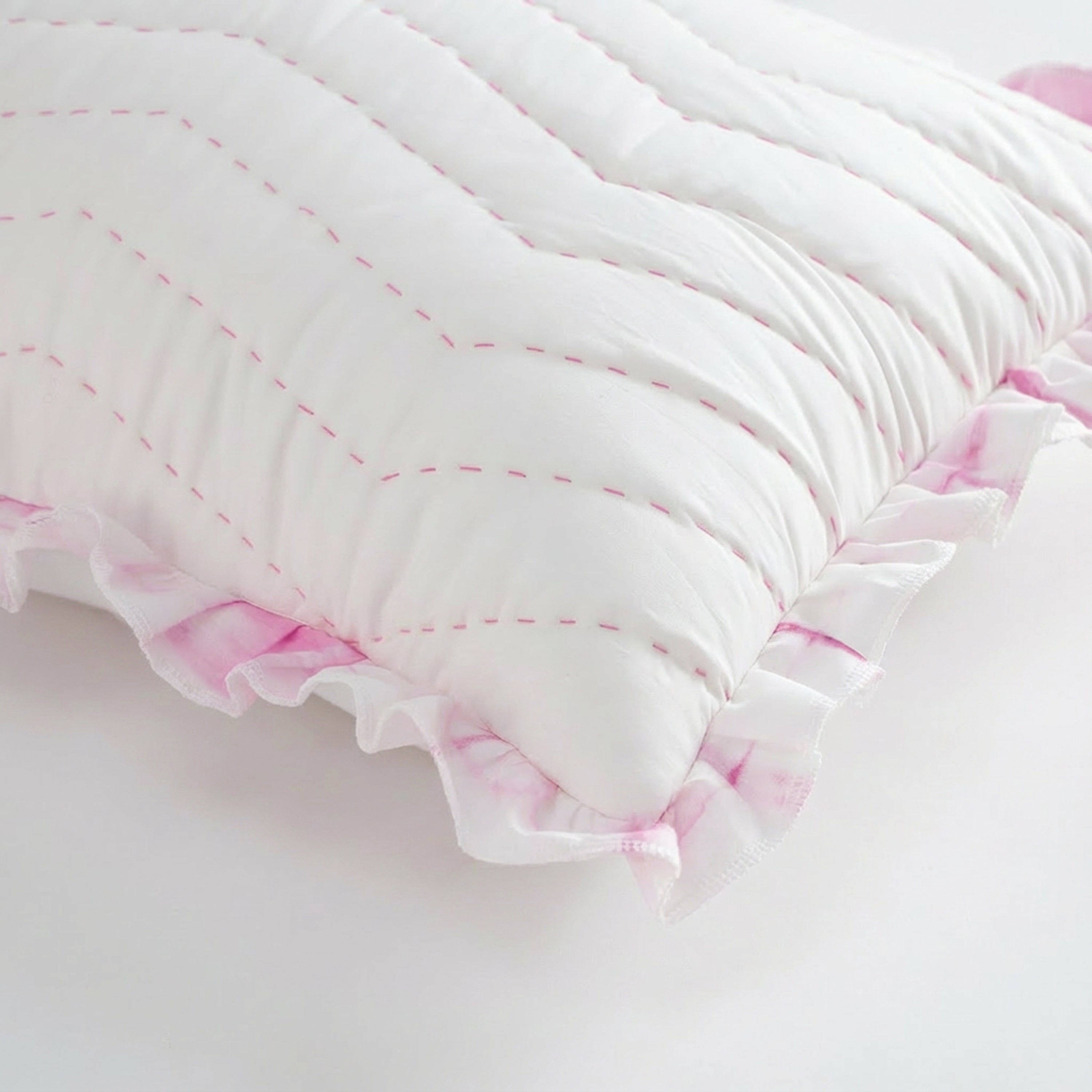 Top-down view of a pink tie-dye ruffle chevron cotton pillow cover for a trendy dorm room or living space. Featuring a geometric hand-stitched chevron pattern on white cotton canvas, it is a top choice for layering decorative pillows on a bed or sofa. The soft pink tie-dye accents provide a chic, unique look for personalized home décor. This machine-washable, light-filtering cotton sham is perfect for anyone searching for a high-quality boho chic throw pillow.