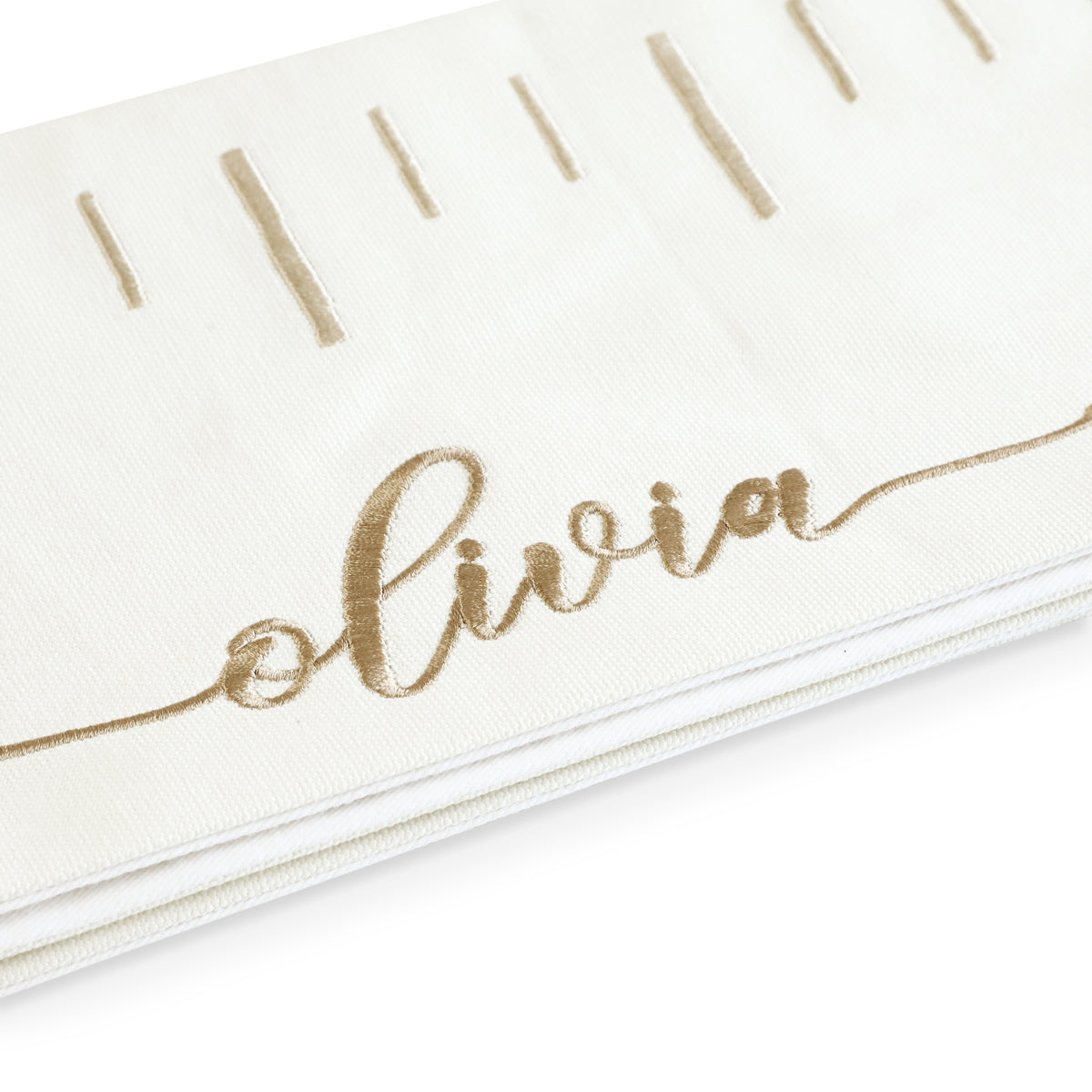 Close-up of a personalized growth chart showing the name Olivia embroidered in script gold thread on white fabric.