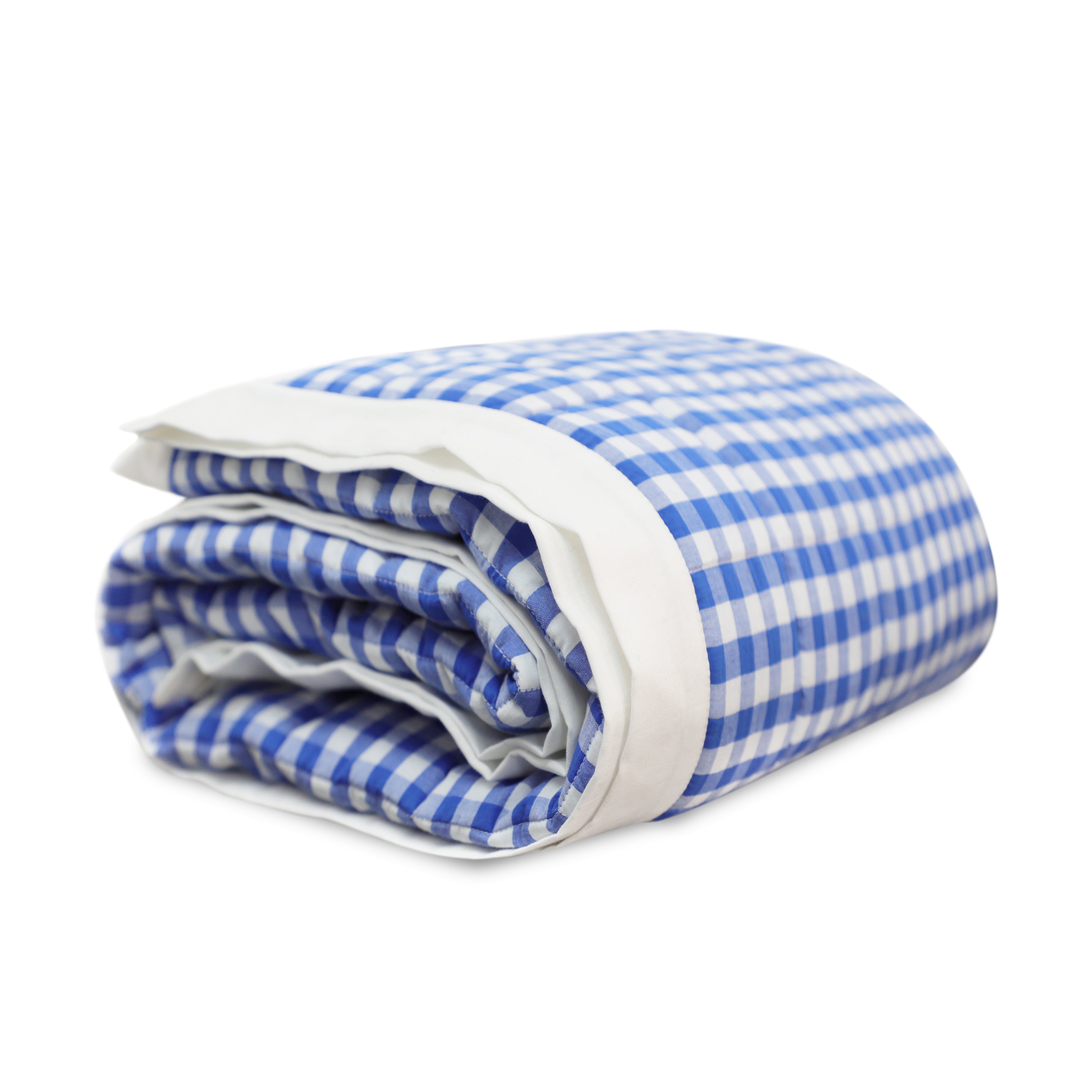 A blue and white gingham cotton quilt rolled up. The pick stitch quilt is accented with white flange on all sides.