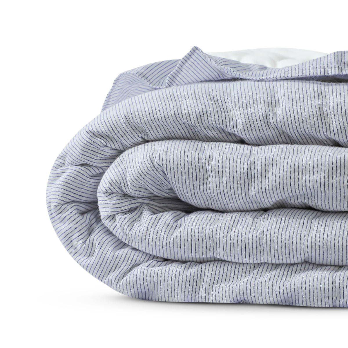 A handmade blue and white striped cotton quilt with ruffles, laid out on a bed in a bright room.