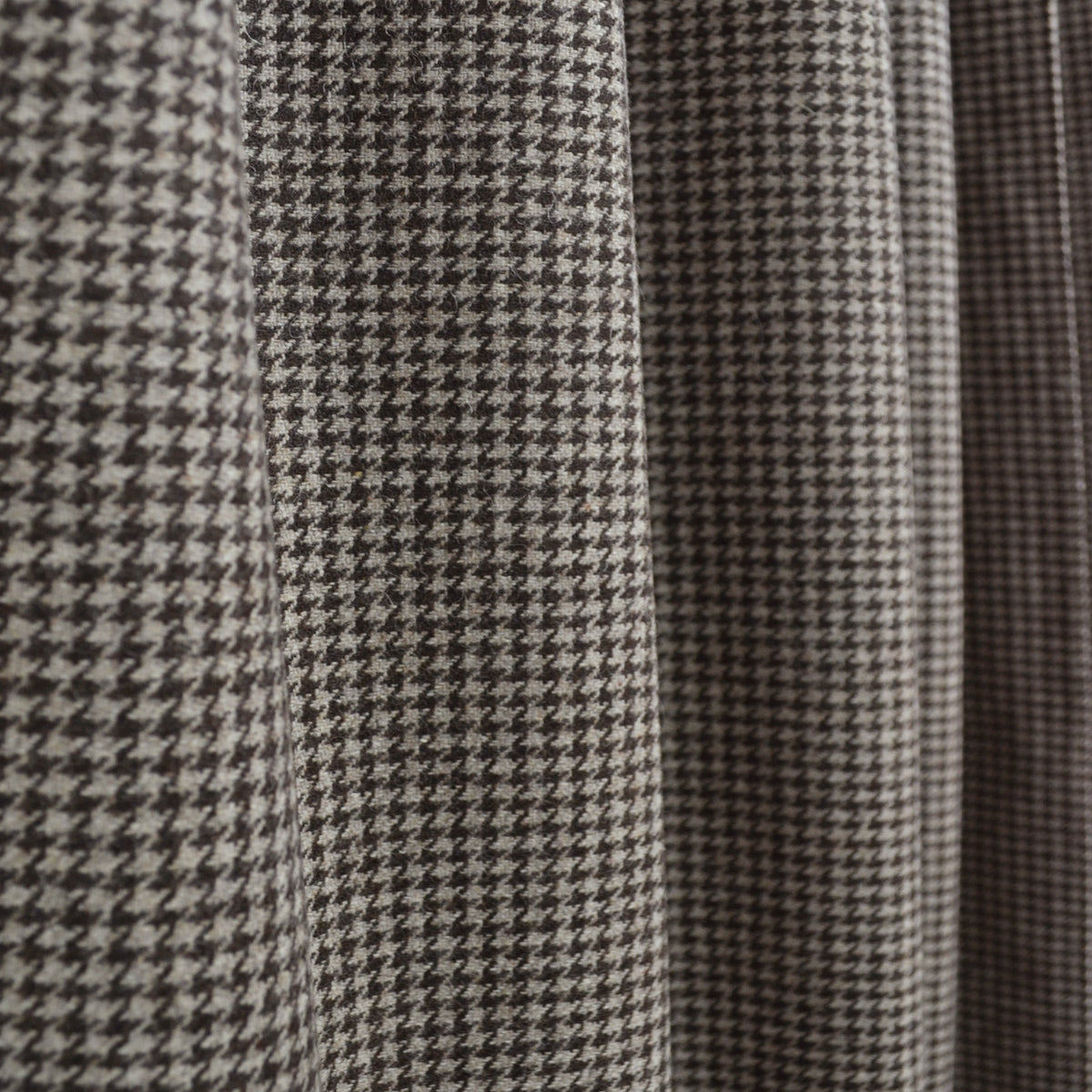 A close-up section of a houndstooth wool curtain with leather tabs and snap buttons hanging on a curtain rod.