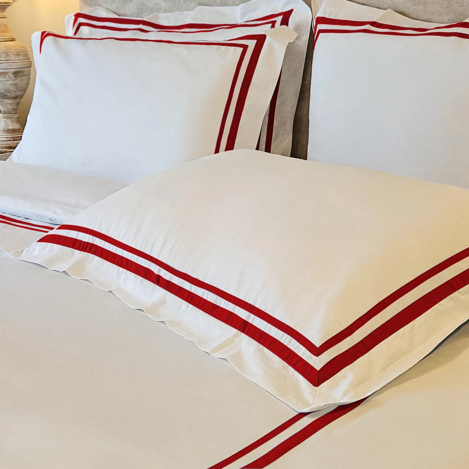 White luxury cotton duvet cover set and matching pillow shams featuring a bold red double trim border. This 400 thread count cotton blend bedding set by Amore Beauté offers a refined, hotel-style aesthetic for sophisticated bedrooms. The close-up shot highlights the crisp white fabric, durable texture, and vibrant red ribbon detailing. Ideal for eco-friendly home decor, wedding gifts, or a personal luxury bedroom upgrade. Crafted for comfort and style.