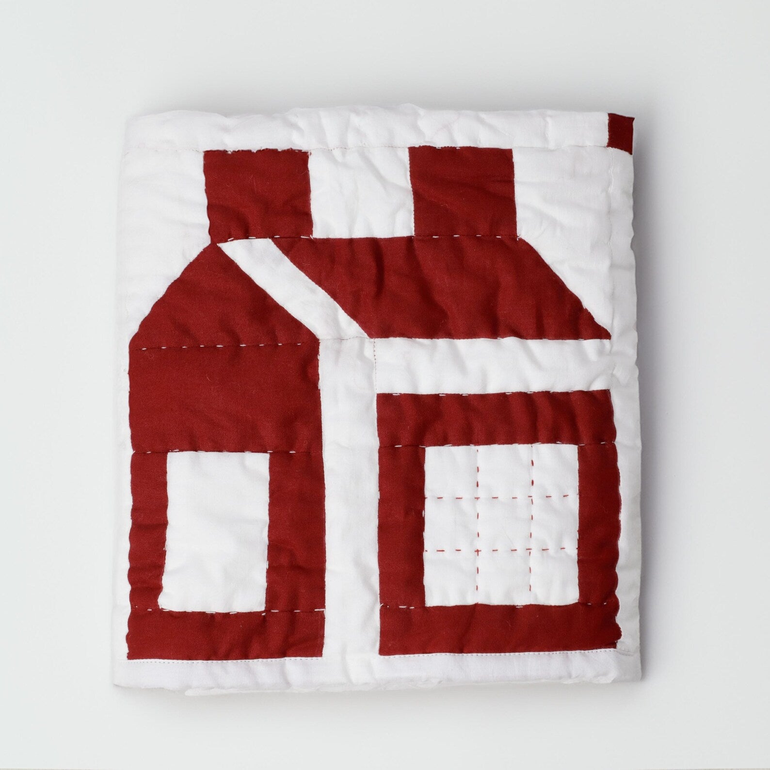 Folded red and white schoolhouse patchwork quilt by Amore Beauté, showing the detailed stitching of this handmade cotton bedding. A popular choice in the US for kids' room decor and traditional interiors, this geometric quilt is also ideal as festive Christmas bedding and holiday home decor. Crafted for a soft, lived-in feel, it fits minimal bedroom aesthetics and spring-summer styles. Available in custom sizes, our designer quilts offer a cozy, warm, and durable alternative to printed linens.
