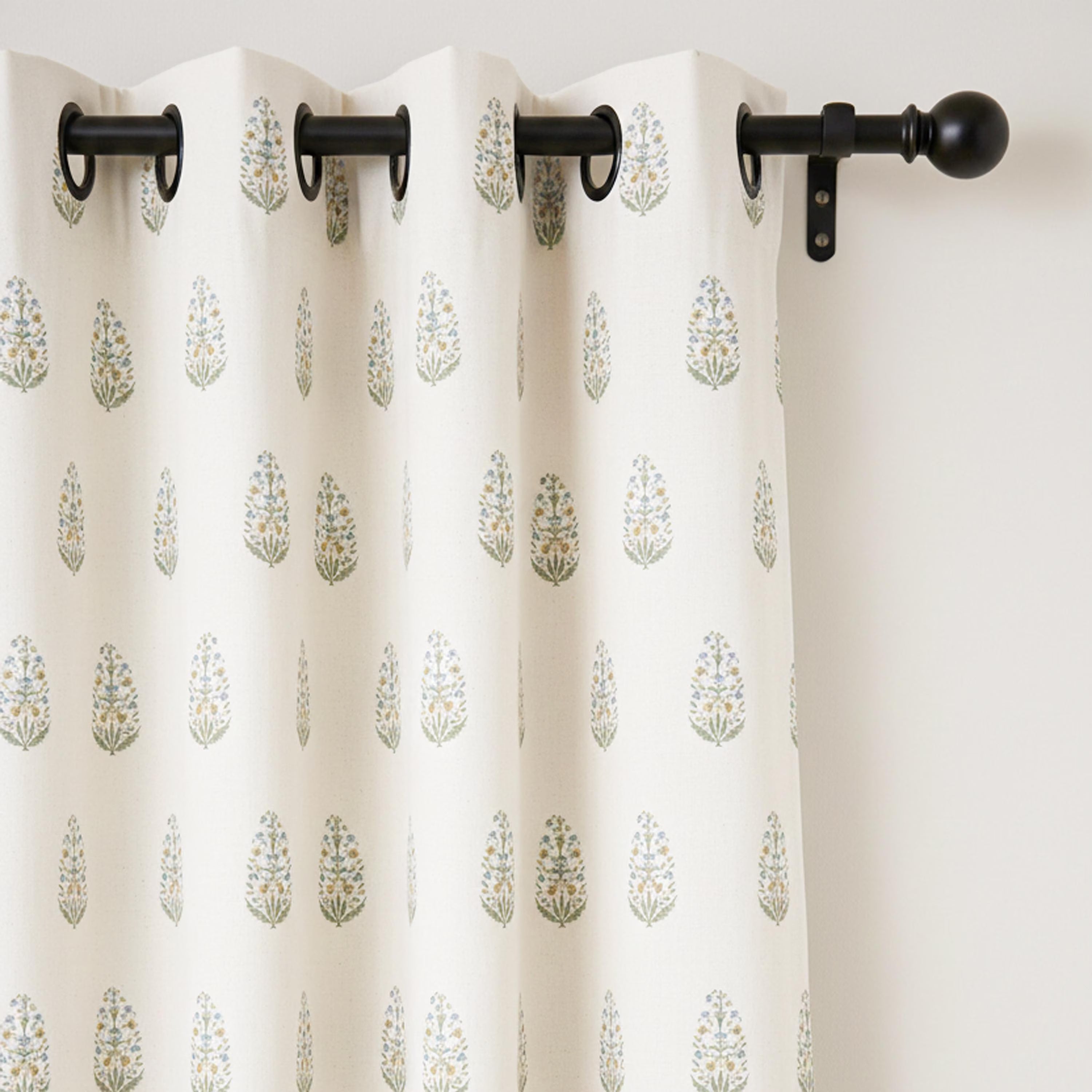 The top section of a block print curtain panel featuring modern black metal grommets hanging on a matching curtain rod. This view demonstrates the clean, structured drape of the medium-weight cotton canvas fabric. These custom drapery panels are designed for easy installation and long-term durability in high-traffic areas like living rooms or boutique hotel spaces. The repetitive floral pattern remains balanced and elegant, fitting perfectly into modern, rustic, or European-inspired window treatments.
