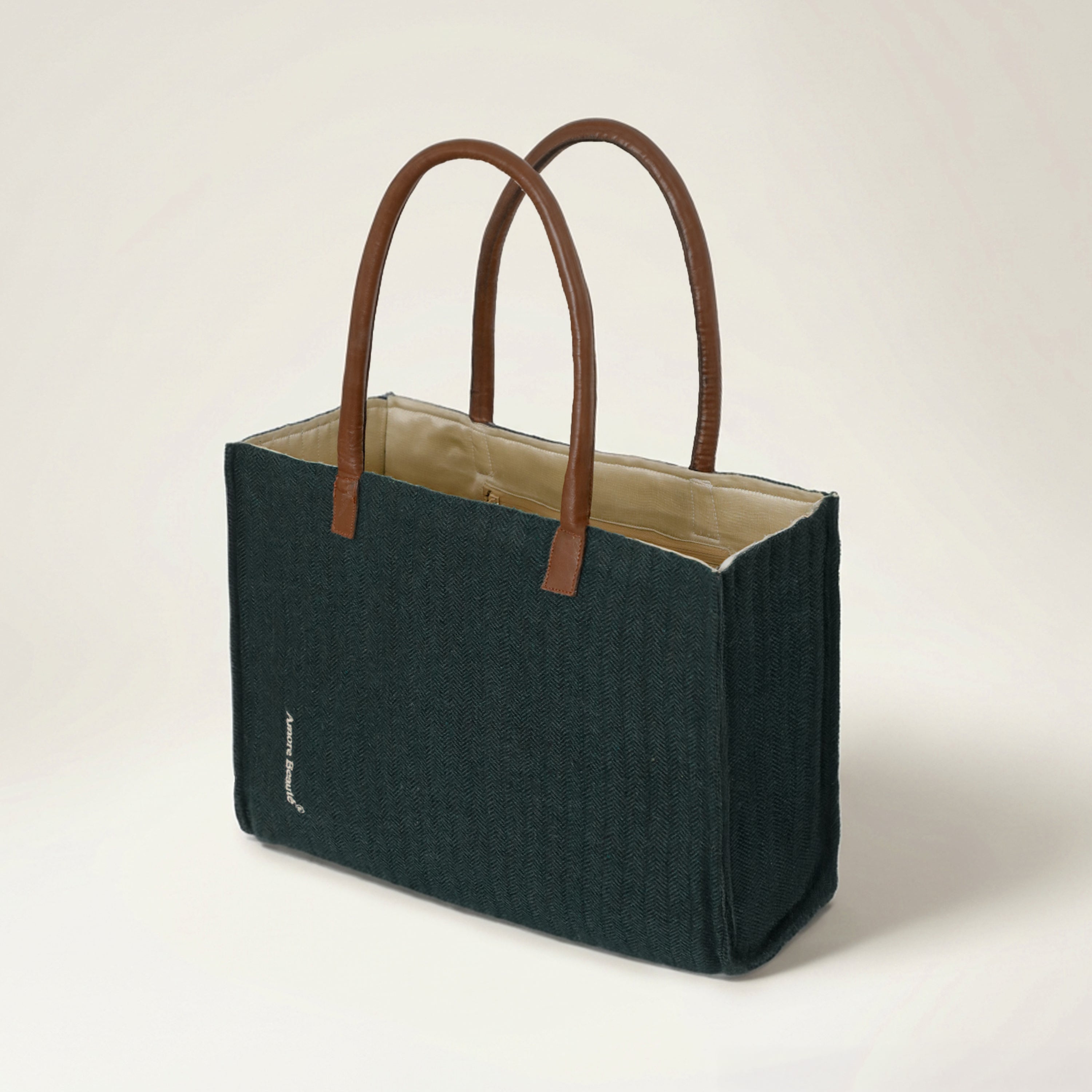 A structured chevron tote bag in a deep forest green textured fabric with premium brown leather handles. This three-quarter view shows the bag's ample depth and ability to maintain its shape, making it an ideal everyday tote for carrying laptops and notebooks. The minimalist, classic silhouette is designed for modern professionals and travelers who appreciate high-quality, non-mass-produced handbags with a standout aesthetic.