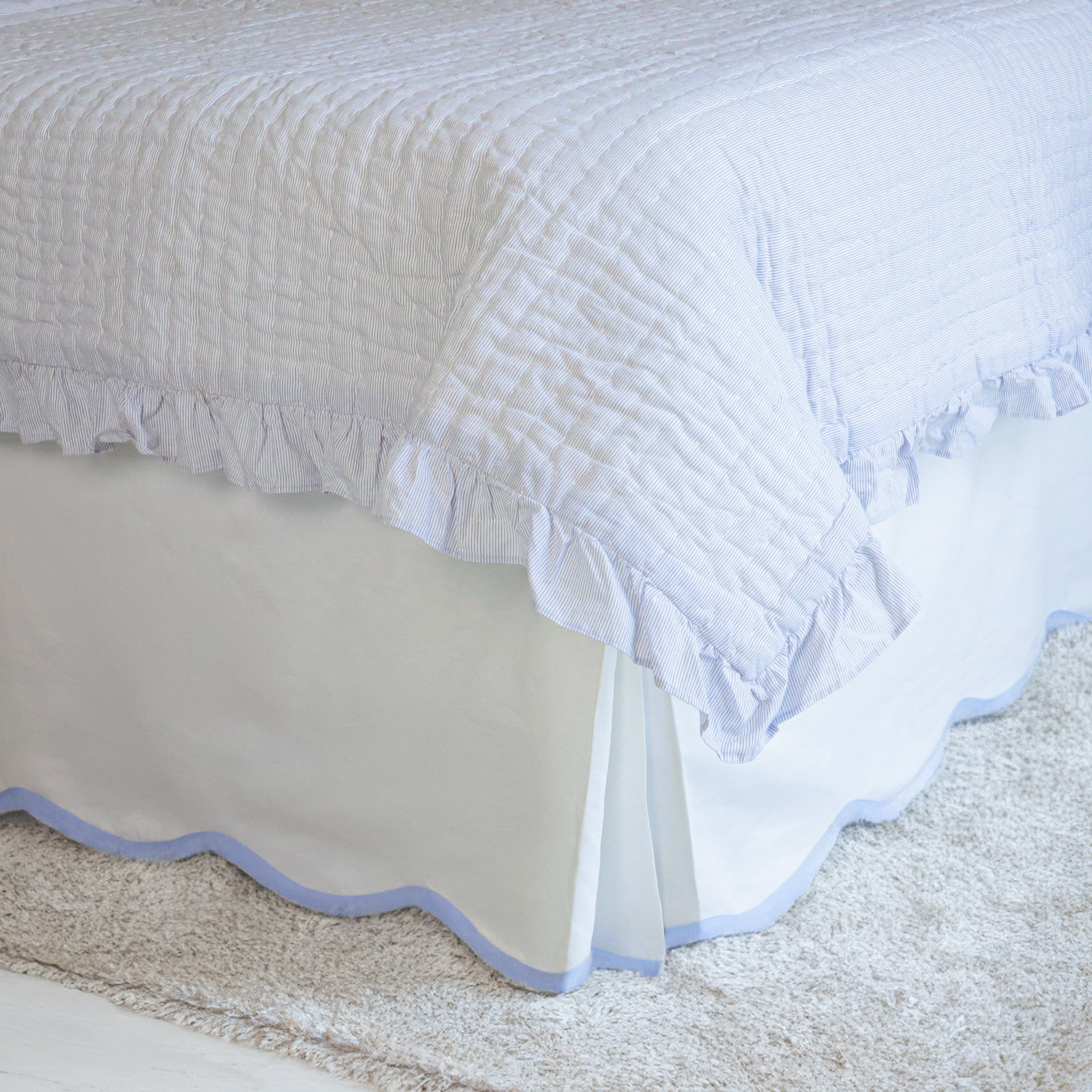 White cotton blend bed skirt with scallop edge on three sides. The bed skirt has a blue trim on three sides.