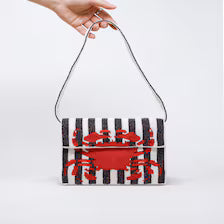 A hand holding a black and white striped Handmade Beaded Crab Clutch with a vibrant red crab pattern.