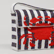 detailed beadwork of the Handmade Beaded Crab Clutch. The textured design features vertical black and white beaded stripes across the front flap, horizontal stripes along the side gusset, and a vibrant red beaded crab motif. 