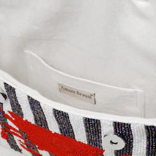 Interior view looking inside the open Handmade Beaded Crab Clutch. The purse is lined with clean, white fabric and features a small inner slip pocket sewn with an "Amore Beaute" brand tag.