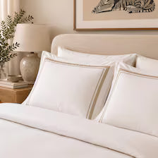 White bedding set with multiple pillows on a bed in a softly lit bedroom setting.