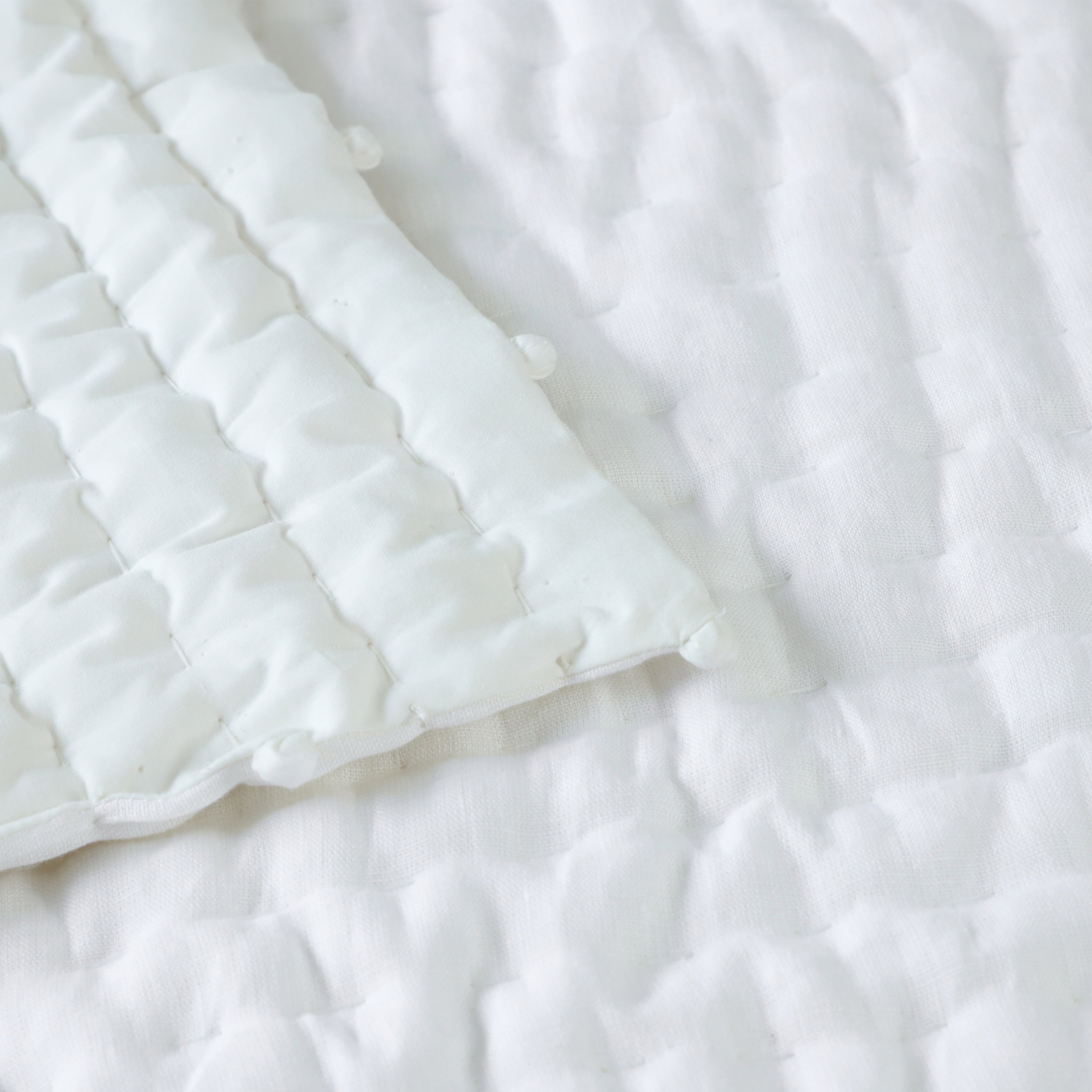 The quilt features an ivory linen top, cotton voile reverse, and cotton batting for warmth, all expertly hand quilted for durability. Shams with a quilted front, pompoms.