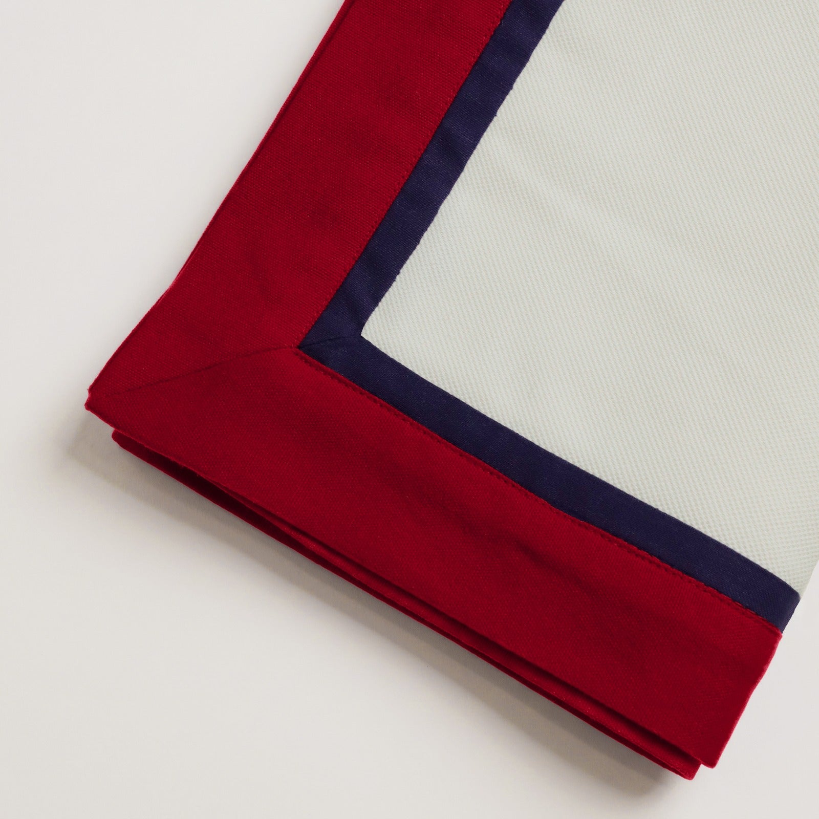 Mitered corner detail of the Ivory Table Runner With Custom Border featuring red and navy blue trim.