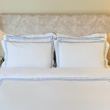 400 Thread Count Satin Cotton Duvet Cover Set with light blue Trim. Four matching white pillows with crisp, parallel light blue embroidered borders.