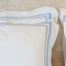 400 Thread Count Satin Cotton Duvet Cover Set with light blue Trim. The clean white cotton shams feature tailored flange edges accented by crisp, parallel light blue embroidered borders along the corners.