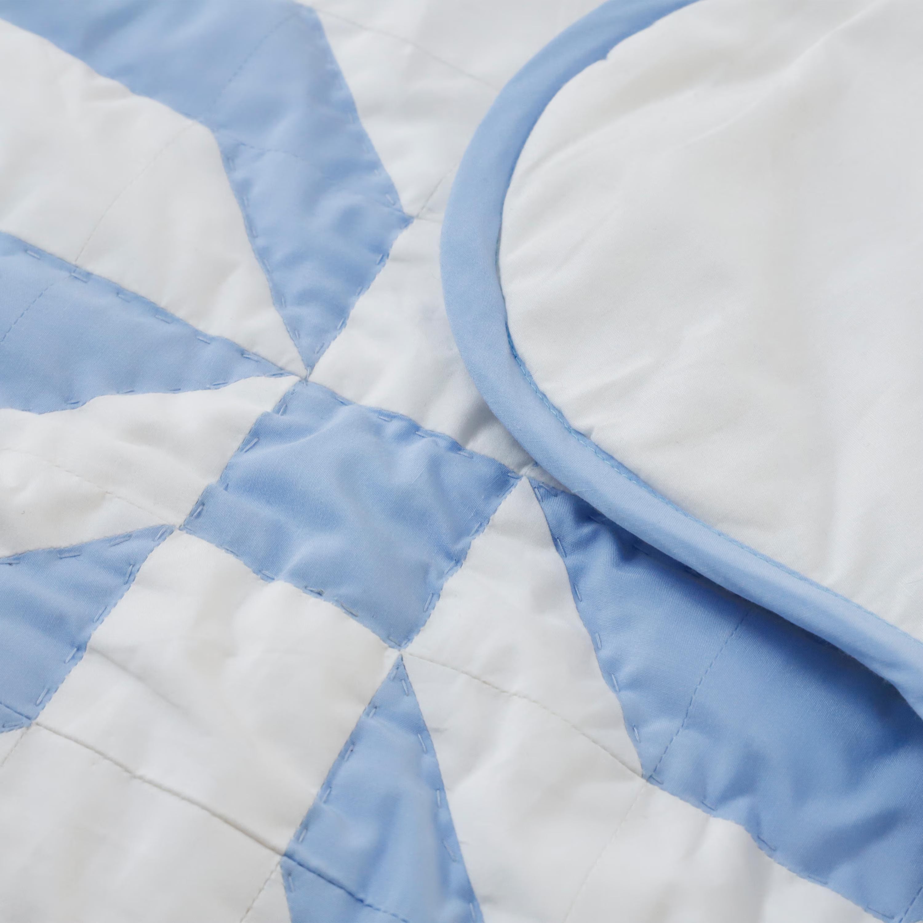 Close-up detail of a blue bow cotton patchwork quilt showing the professional hand-stitched quilting and premium fabric texture. This durable, handmade bedding is designed for lovers of the coquette aesthetic and minimal, preppy room styles. The intricate bow pattern and soft blue tones provide a refined, vintage charm for nurseries and stylish dorm rooms. Amore Beauté ensures heirloom quality in every piece, making this an ideal gift for baby girl rooms or high-end interior design.